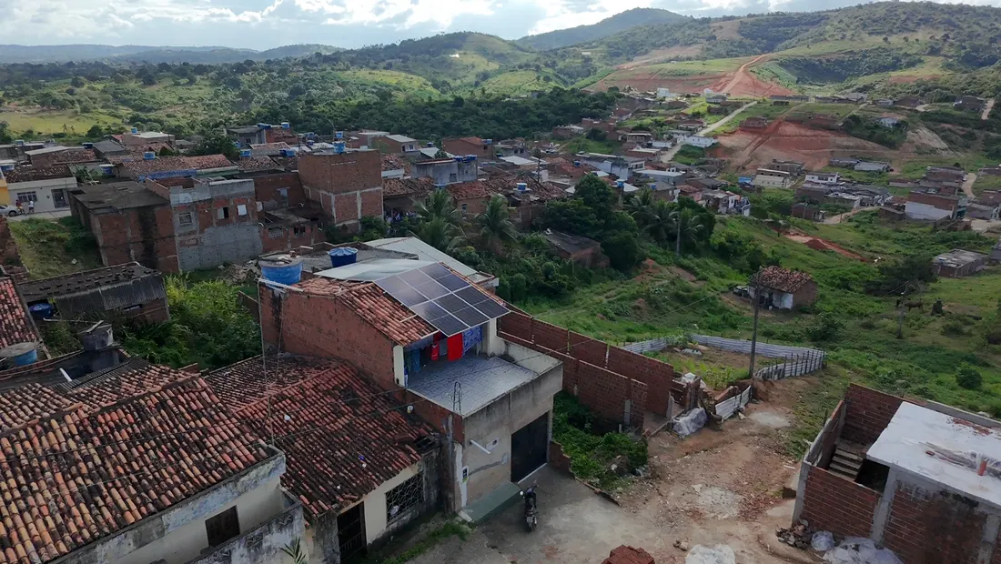 Vista aérea aberta do Loteamento Baú, com a casa do projeto, o bairro e os morros ao fundo